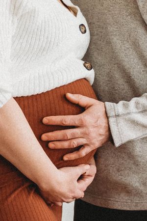 Close-up of hands tenderly cradling a pregnant belly in brown dress.