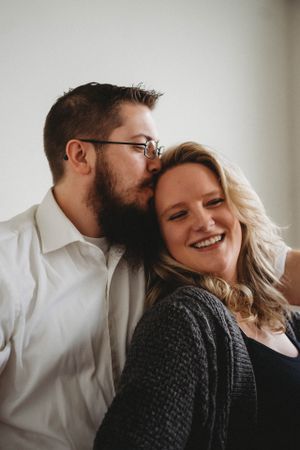 Intimate portrait of couple sharing a sweet moment against white wall.