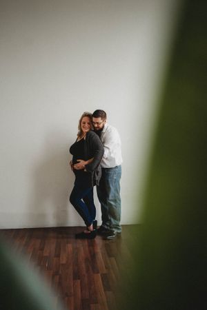 Artistic maternity photo through foliage showing couple embracing.
