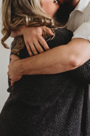 Close-up of embrace showing arms wrapped in warm sweater against neutral background.
