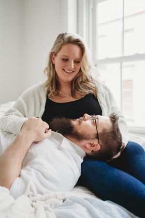 A tender moment between a couple relaxing on white bedding near a sunlit window.