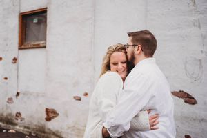 Romantic outdoor portrait against a white building wall in natural lighting.