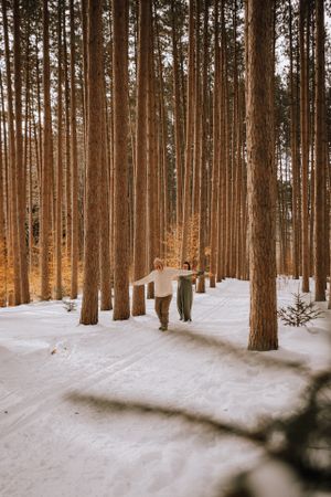 A couple walking hand in hand through a snow-covered pine forest path.