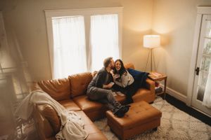A tender moment shared on a brown leather couch in a warmly lit living room.