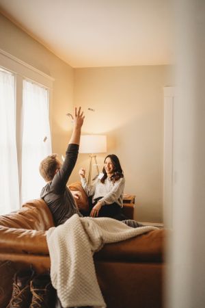 Playful scene on a leather couch with arms reaching up near a table lamp.