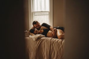 Sunlit bedroom scene through doorway showing tender moment on bed.