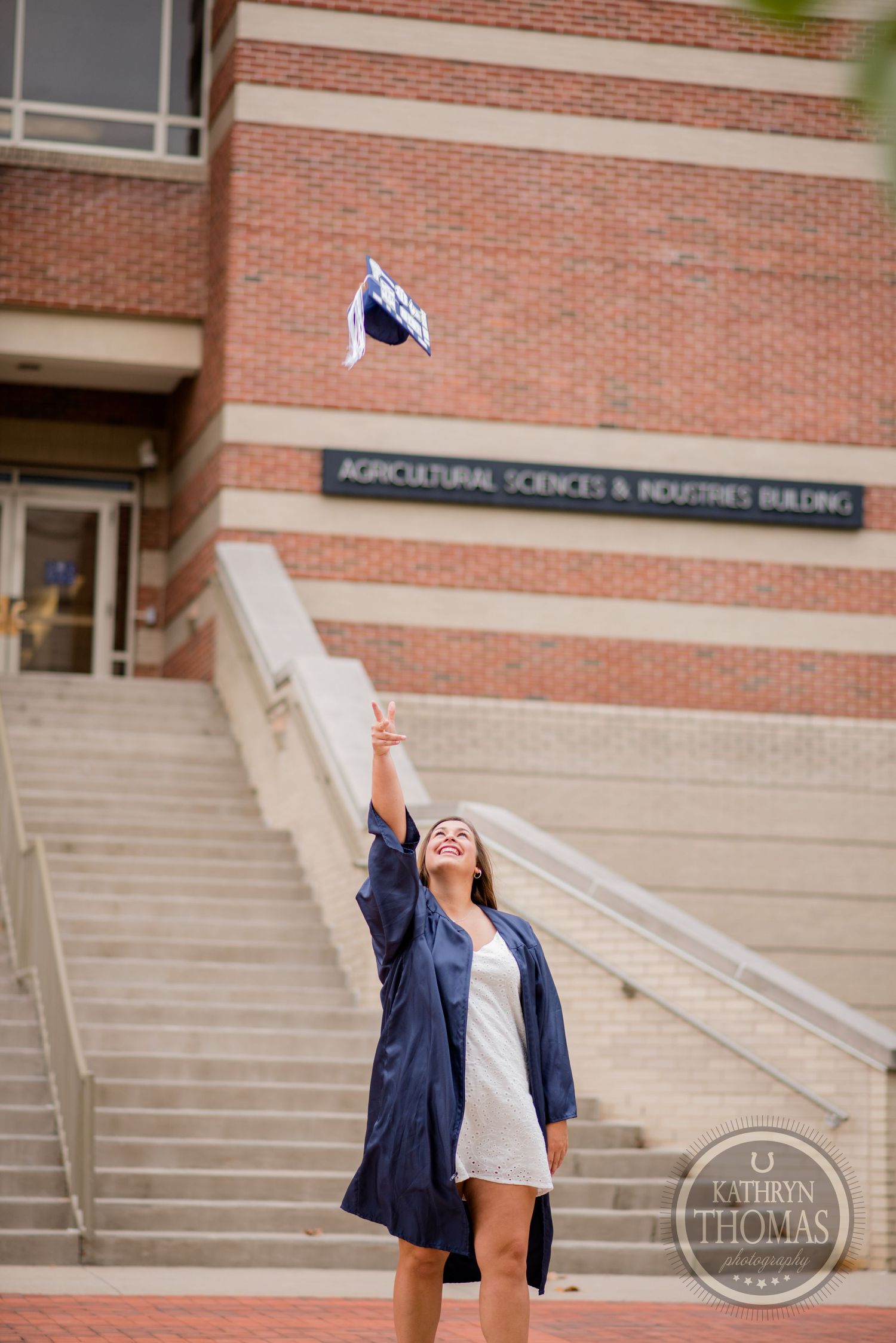 A graduating student joyfully throws their cap in the air on the steps of an academic building.