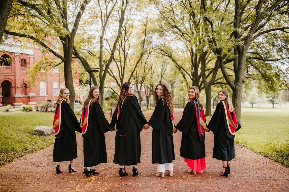 Group graduation photo with black gowns and red stoles in outdoor campus setting.