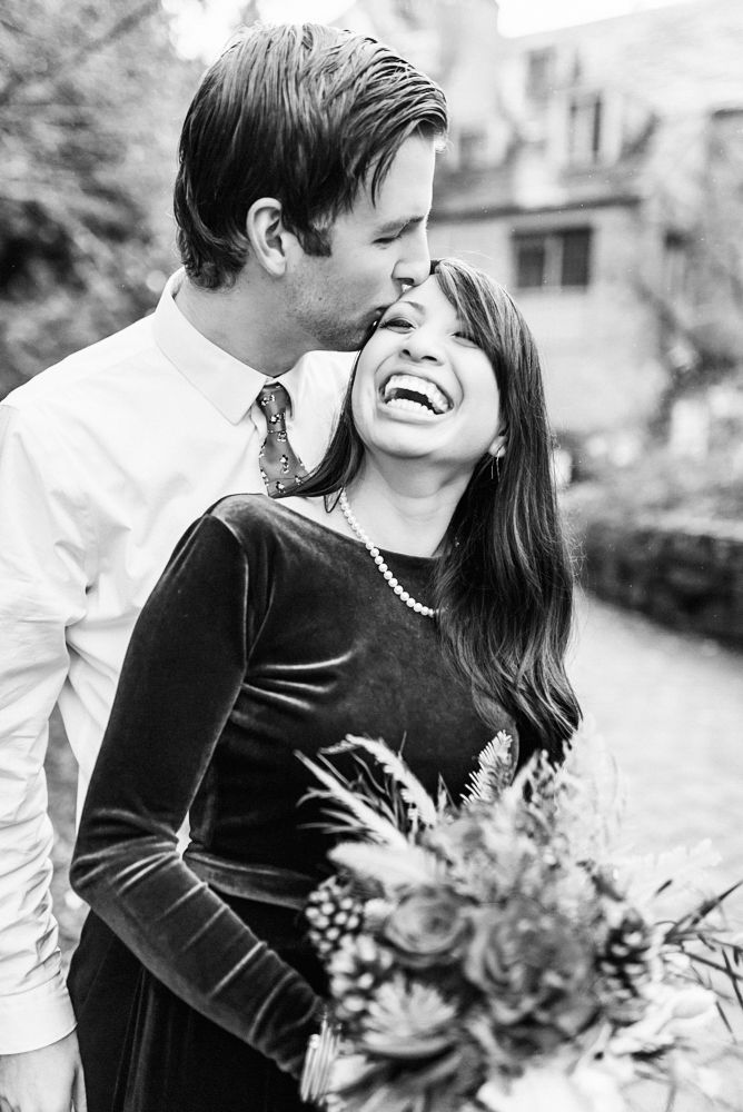 A joyful black and white moment of a couple sharing laughter with a floral bouquet.