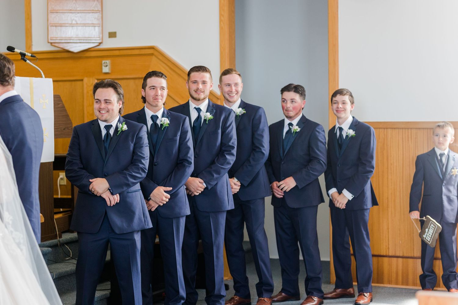 Groomsmen lined up in matching navy suits inside church sanctuary.