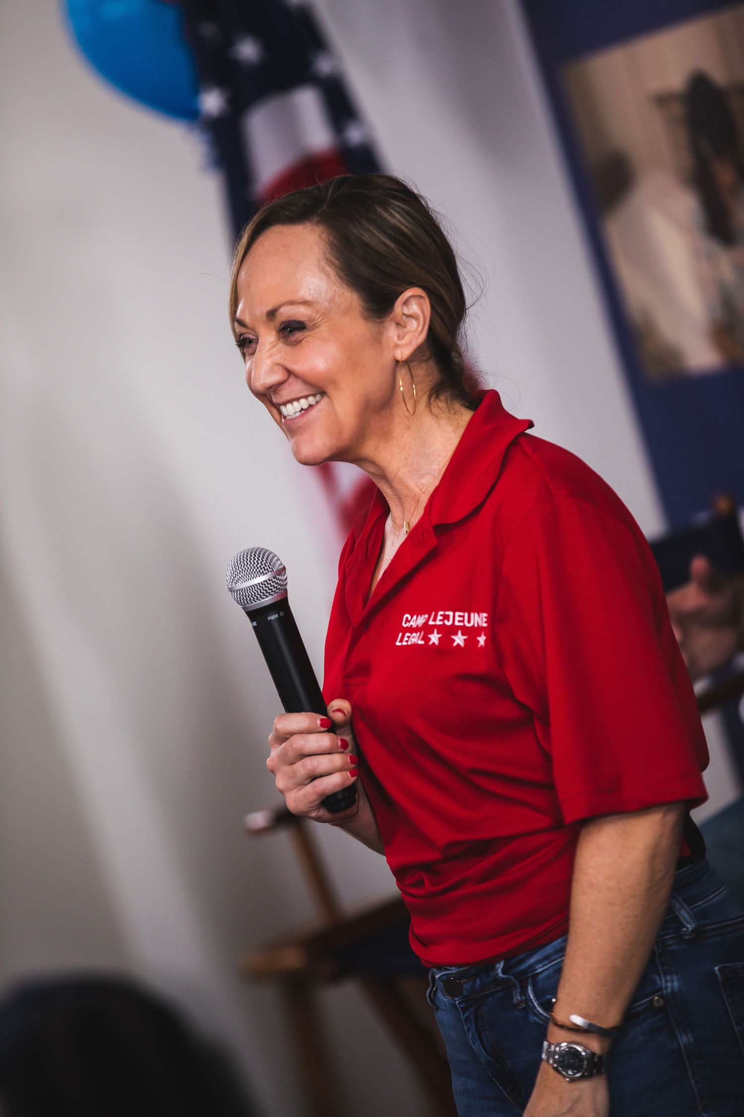 A speaker holds a microphone while wearing a red polo shirt at a political event.