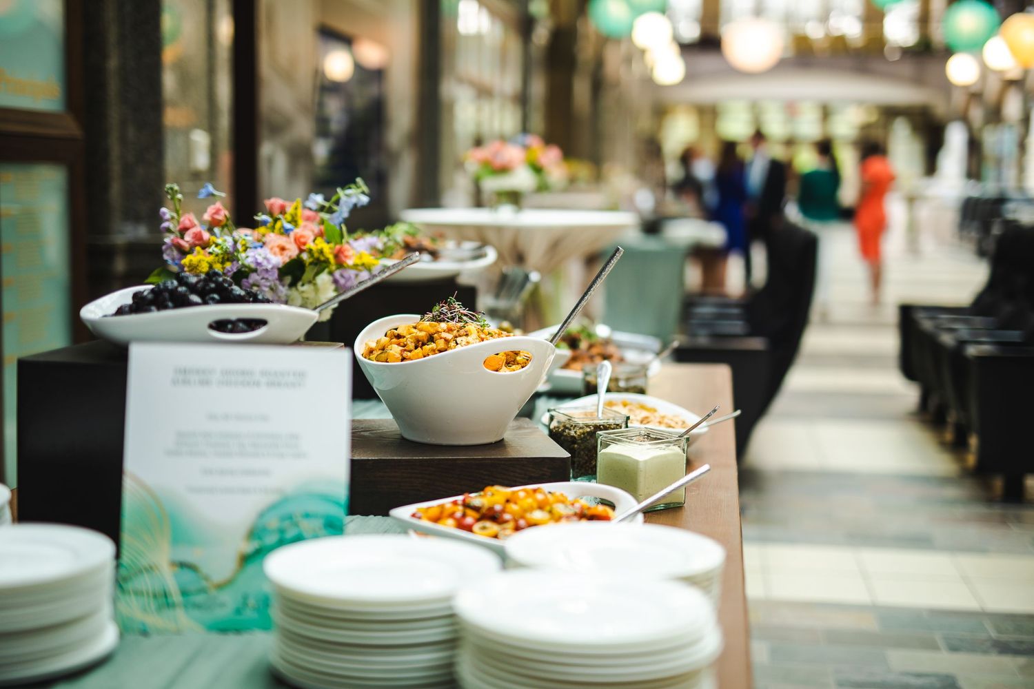 Buffet spread of various dishes and appetizers displayed in white bowls with fresh flowers.
