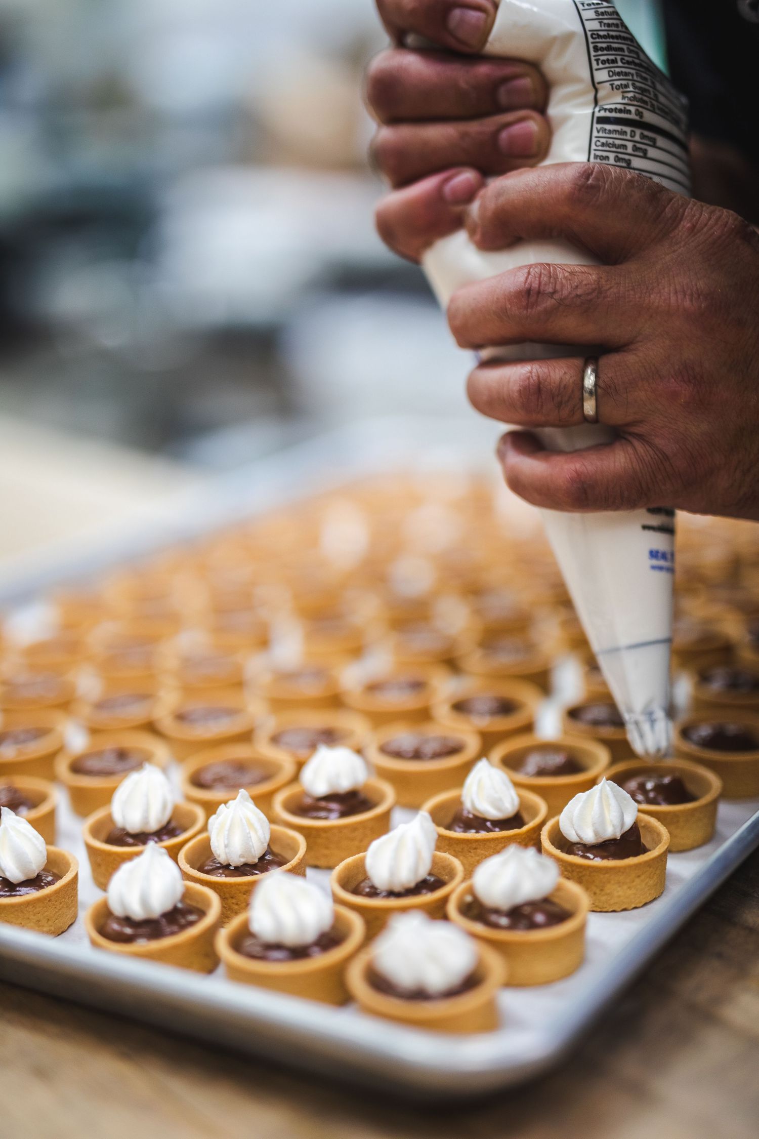 Close-up of hands piping white frosting onto small round pastries.