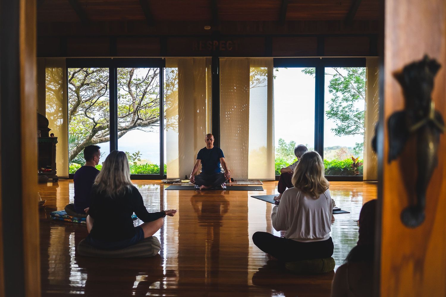 Silhouettes of people meditating in a serene studio with mountain views.