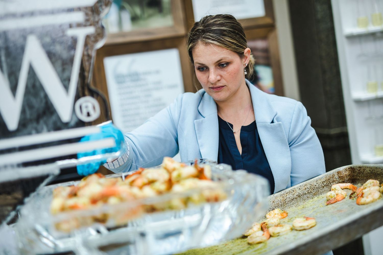 Someone in light blue blazer arranging catered food on serving trays.