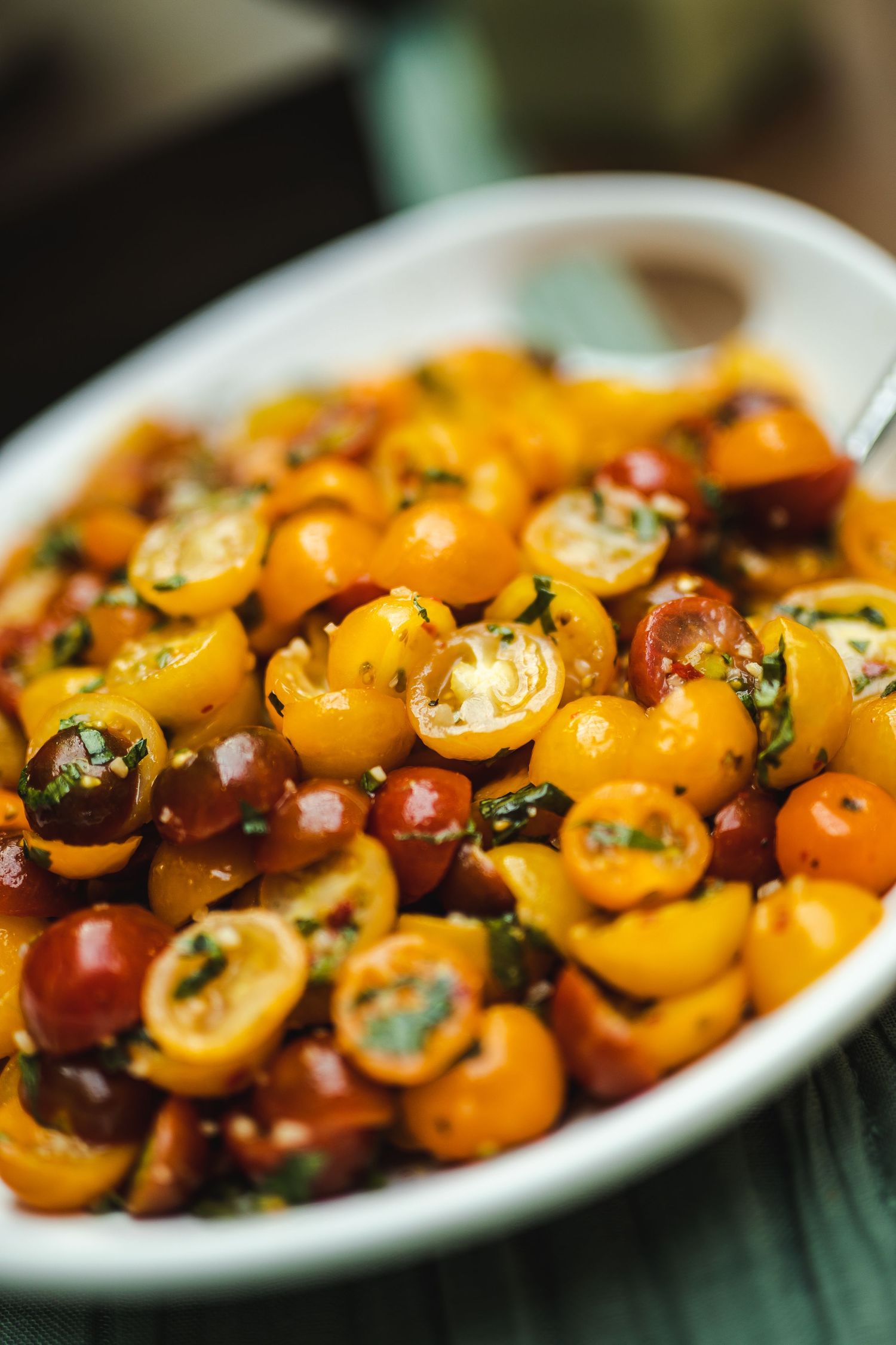 Colorful cherry tomatoes marinated with herbs and seasonings served in a white bowl.