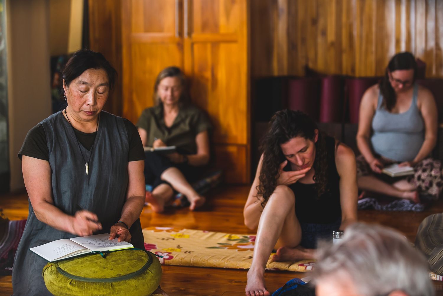 Group meditation or mindfulness session in wooden room with participants sitting on floor.