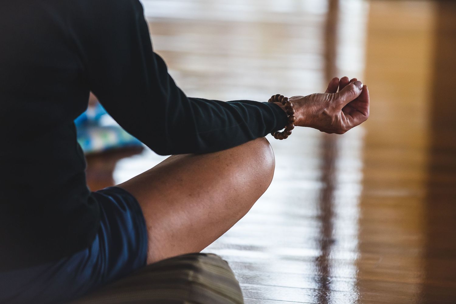 Close-up of crossed legs in meditation pose on wooden floor.