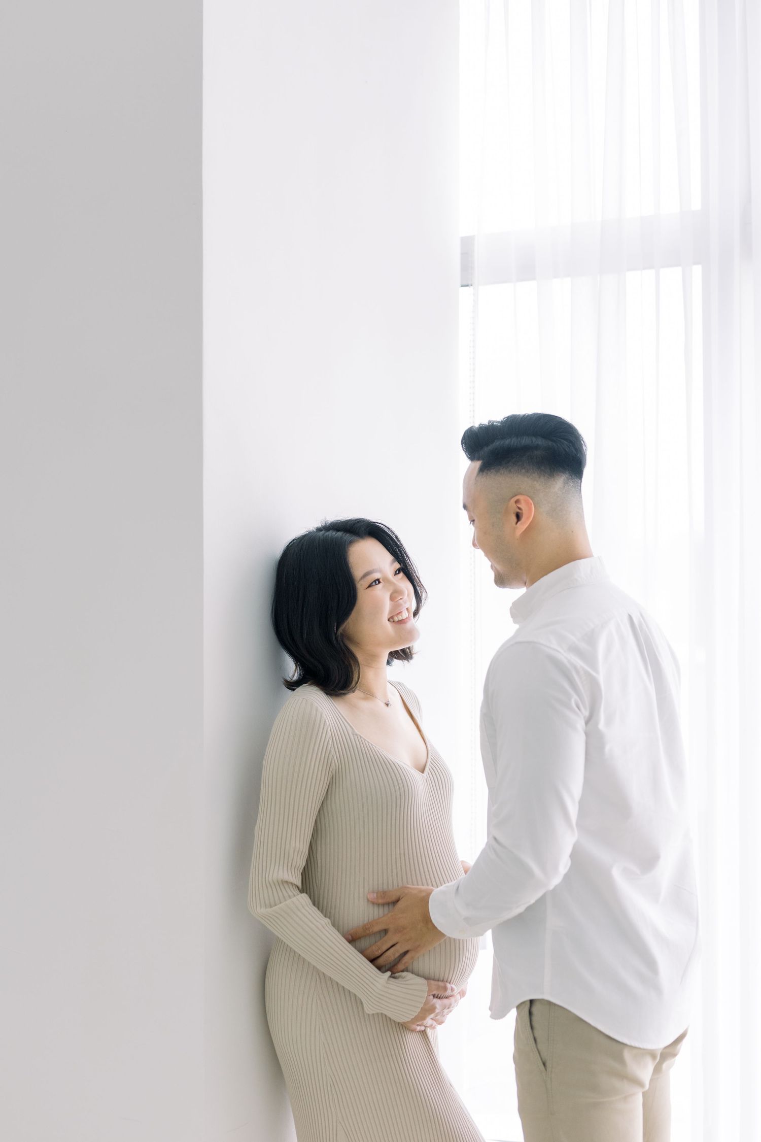 Intimate maternity photo of a couple by a bright window.