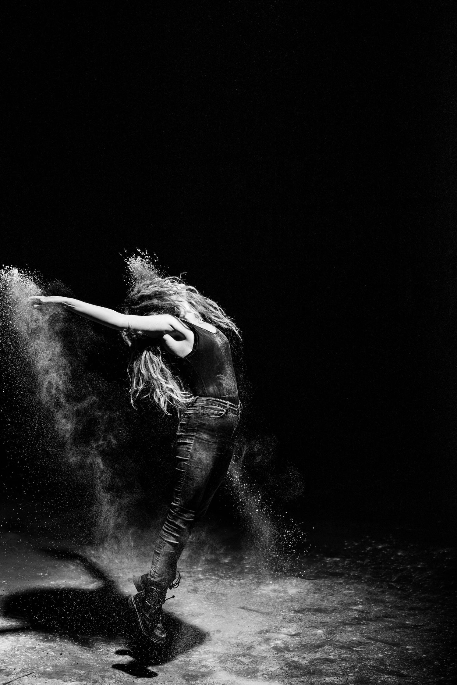 A dramatic black and white photo of a dancer leaping through powder in the darkness.