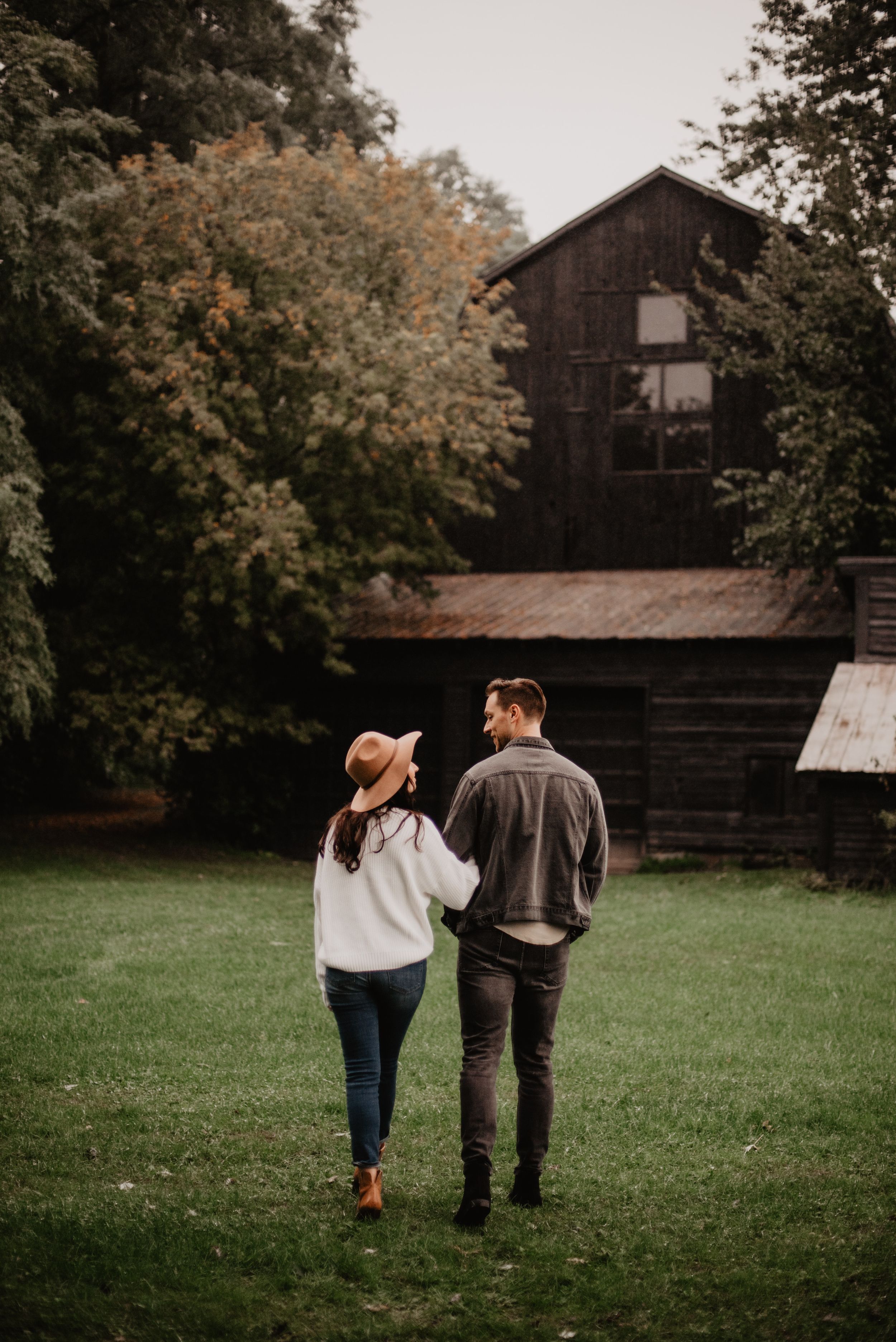 Couple looking at each other in front of a cabin while she's holding his arm