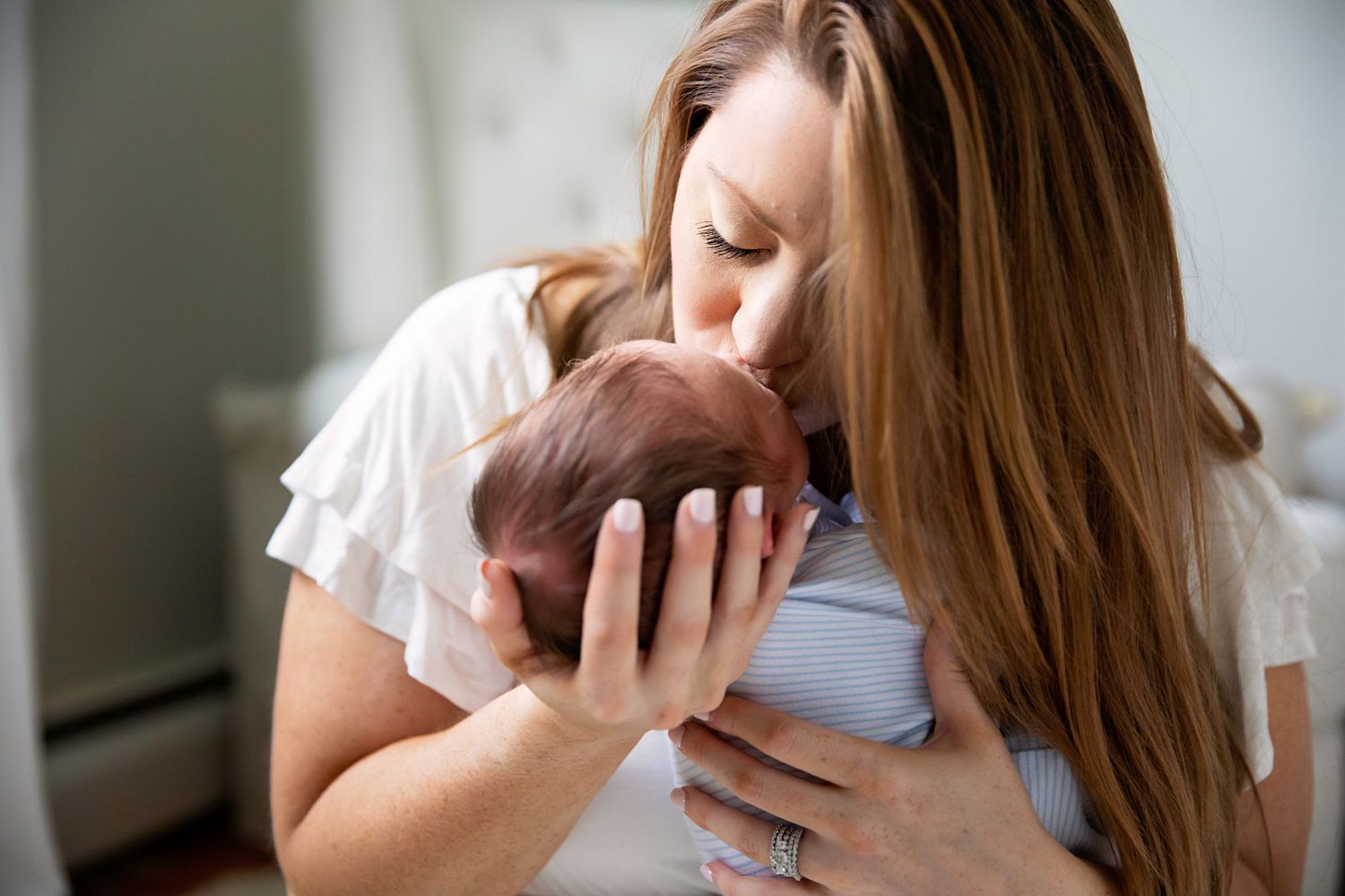 Parent gently kisses newborn baby in intimate indoor portrait.