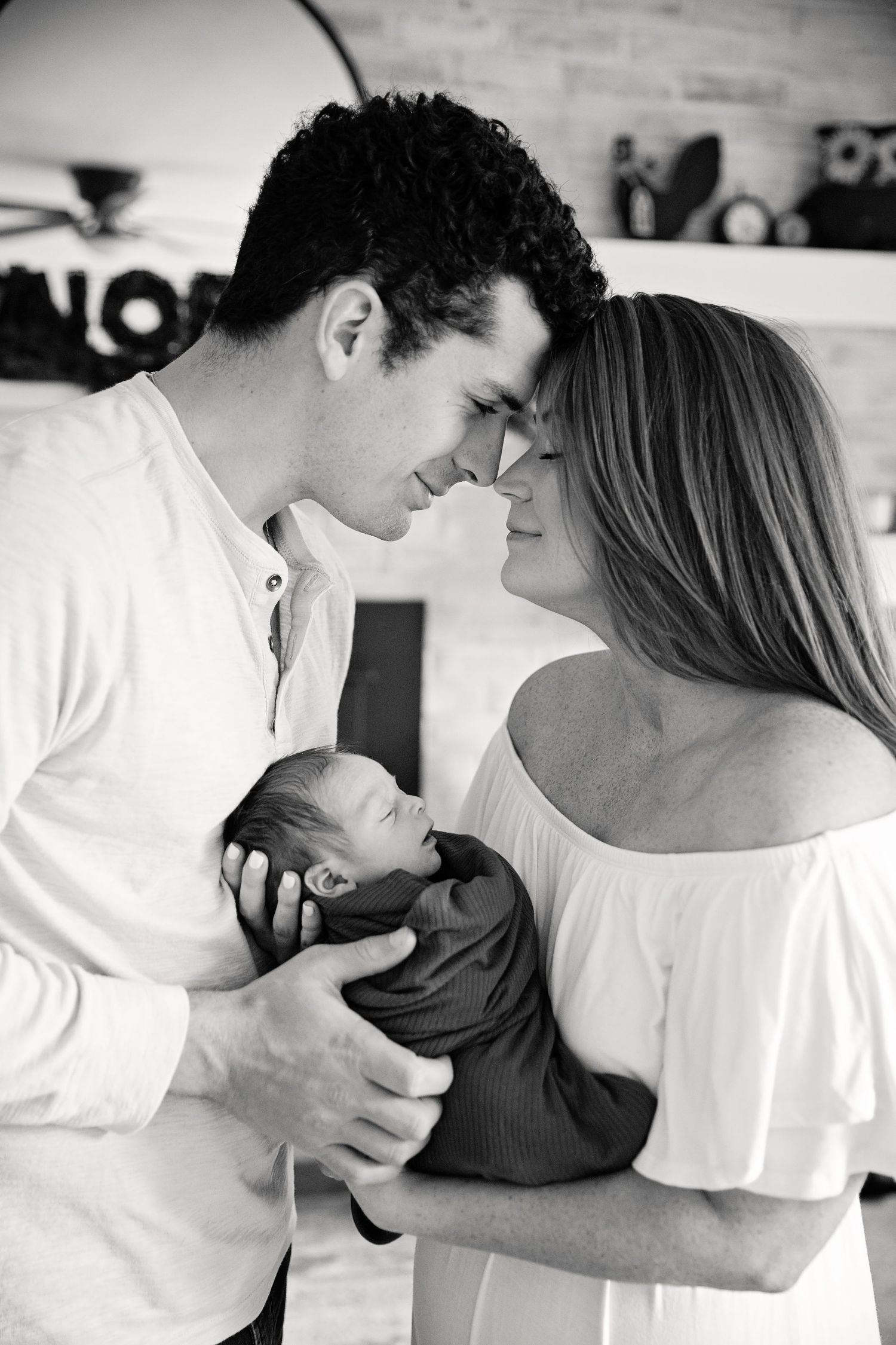 A tender black and white portrait of new parents sharing an intimate moment while holding their newborn baby.