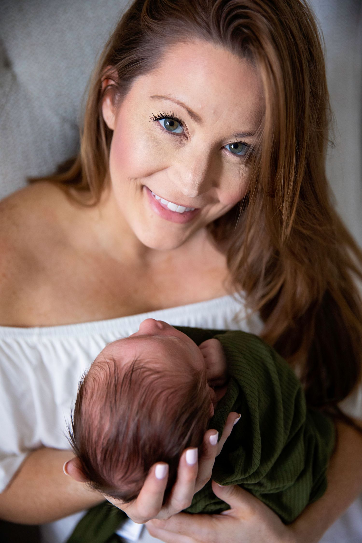 Parent holding newborn baby wrapped in green blanket against gray background.