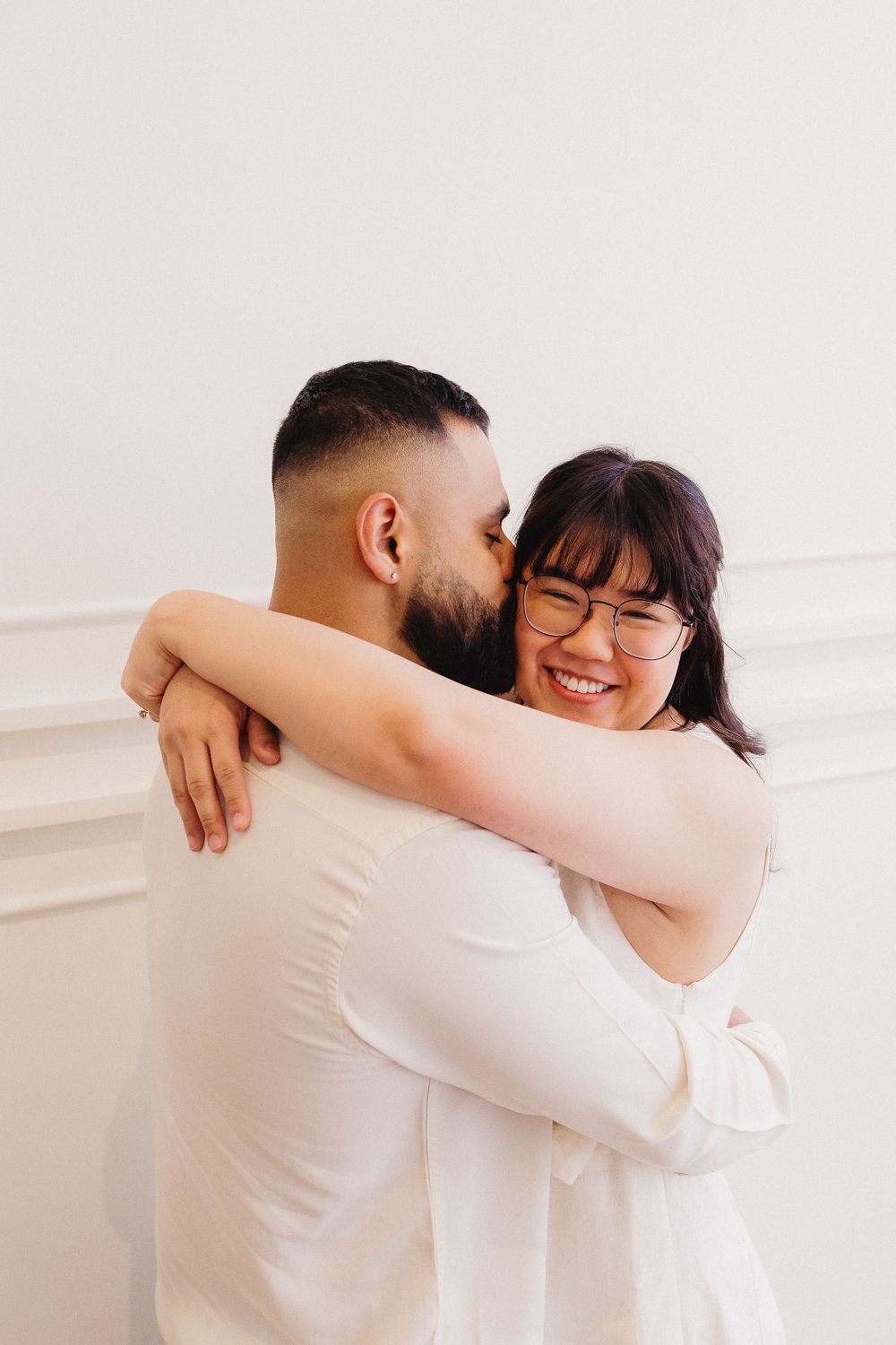 Couple sharing warm embrace against white wall in casual attire.