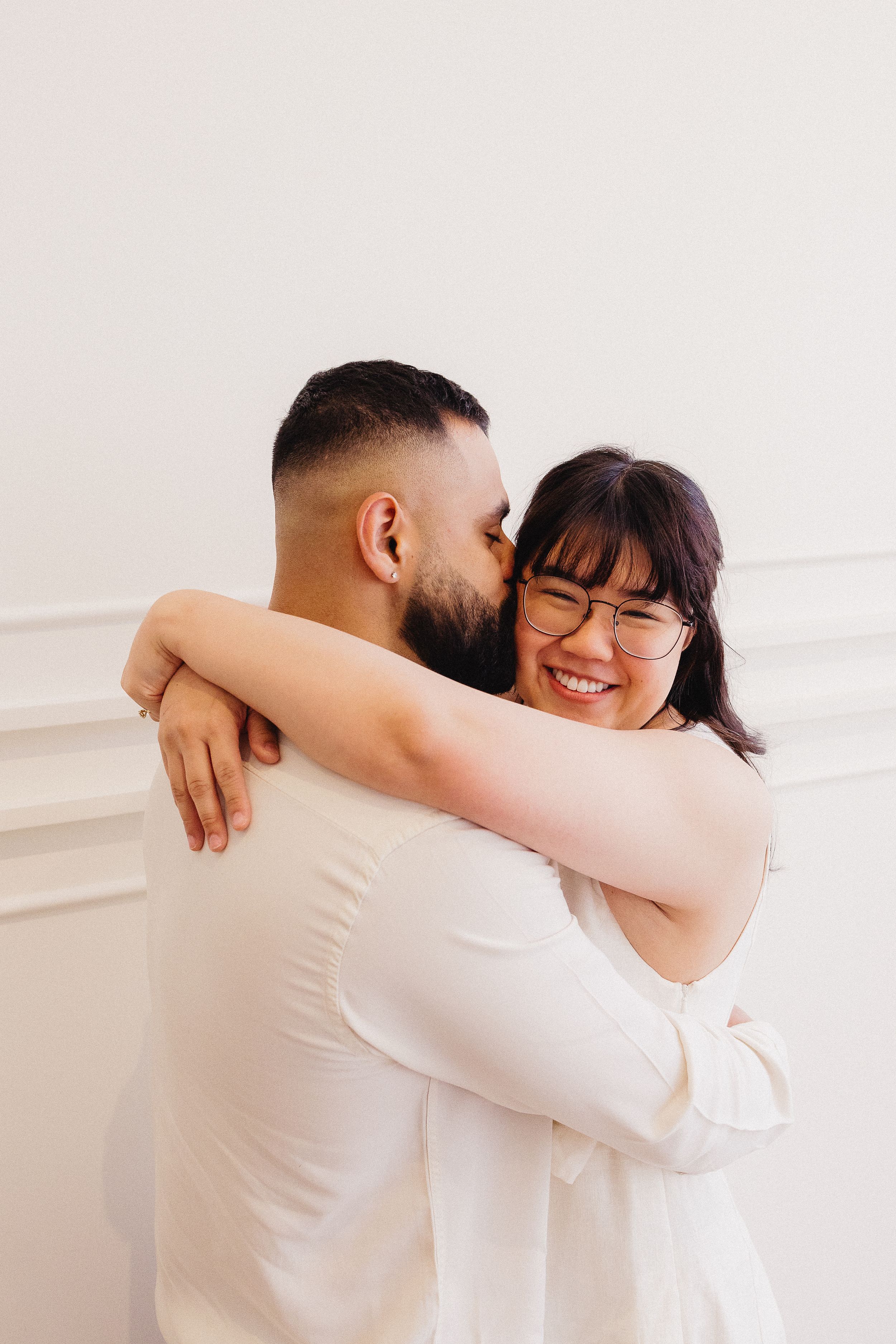 Couple sharing warm embrace against white wall in casual attire.
