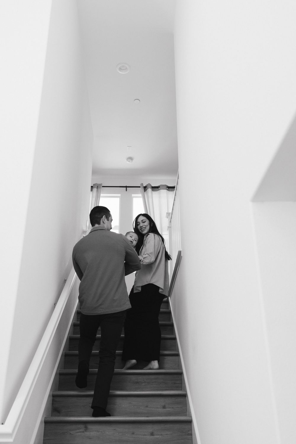 Black and white photo of two people interacting on a stairwell in a bright, modern interior space.