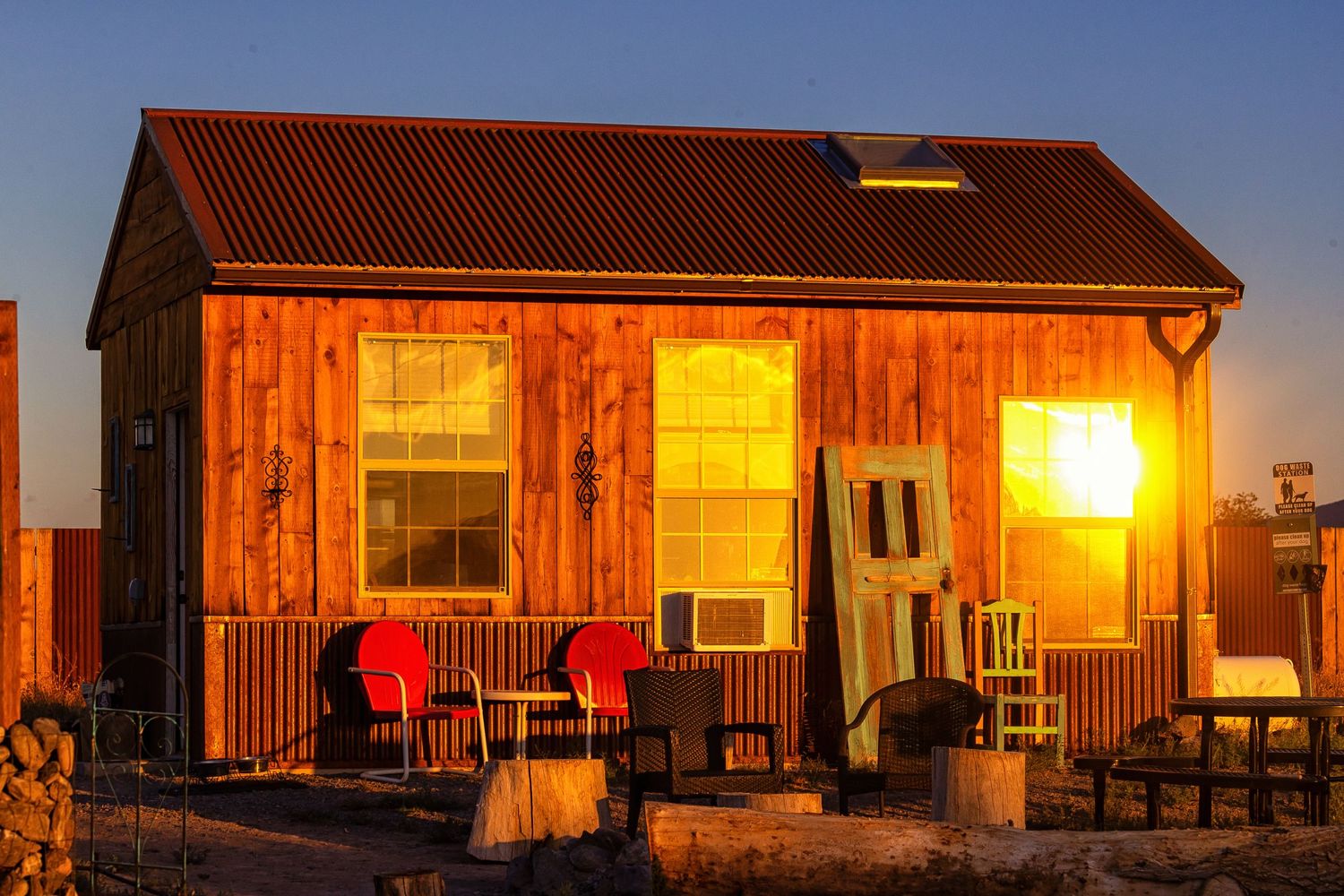 Rustic wooden barn exterior glowing warmly at sunset with red chairs on the porch.