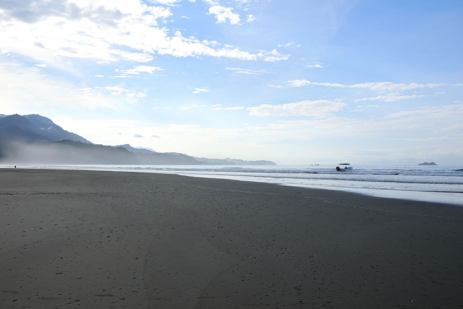 Misty morning on a black sand beach with mountains in the distance.