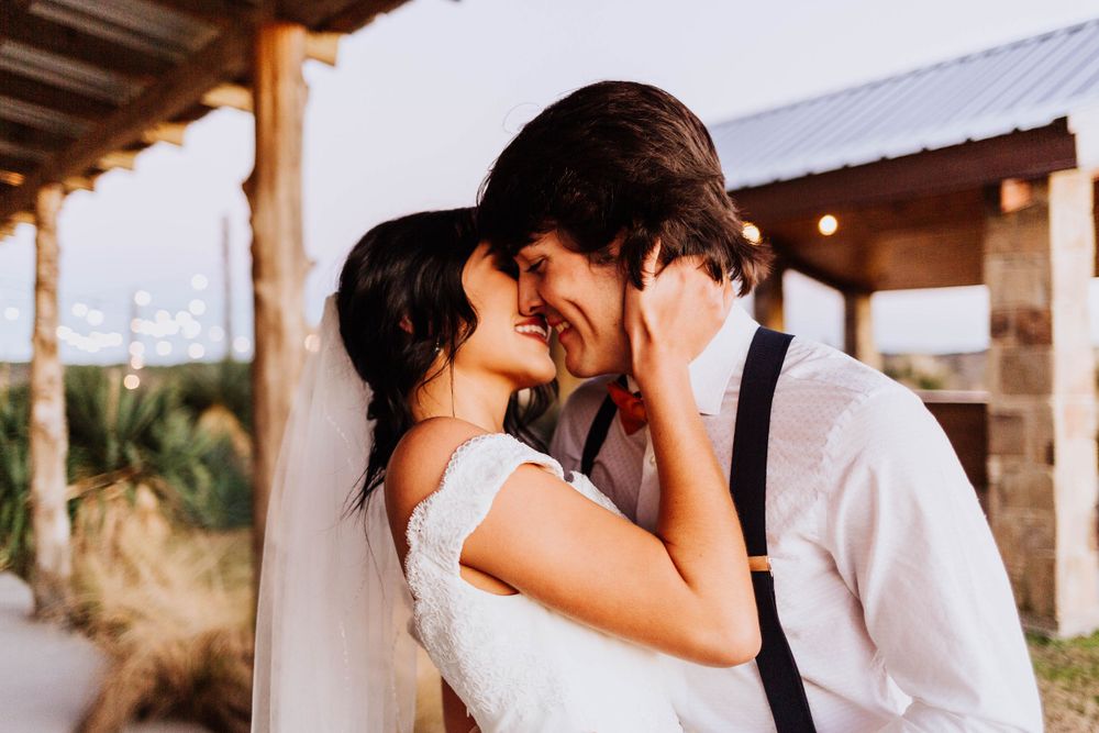 Bride and groom share intimate nose-to-nose moment under rustic wooden venue at outdoor wedding.