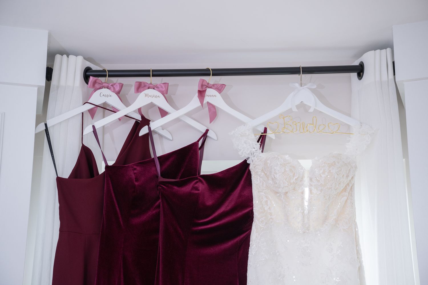 Burgundy velvet bridesmaid dresses hanging beside white wedding gown on clothing rack.