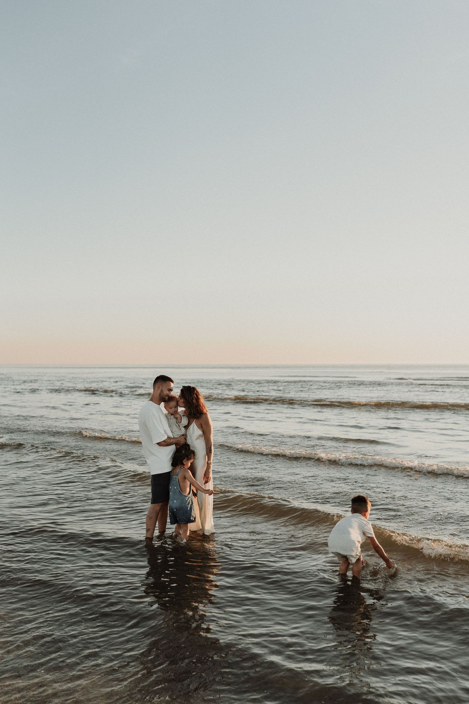 Family playing together in ocean waves at sunset on sandy beach.