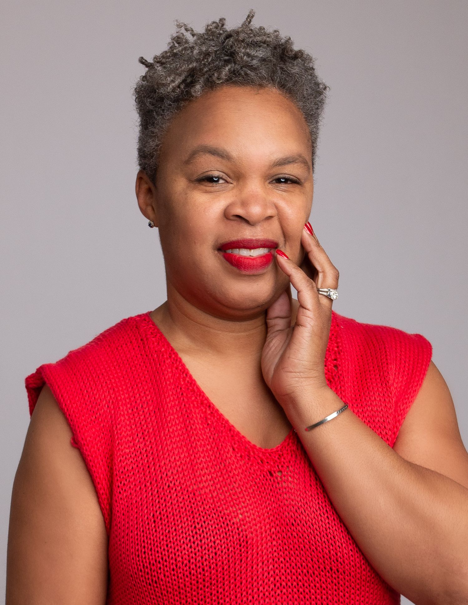 Professional headshot in bright red sleeveless top against gray background.