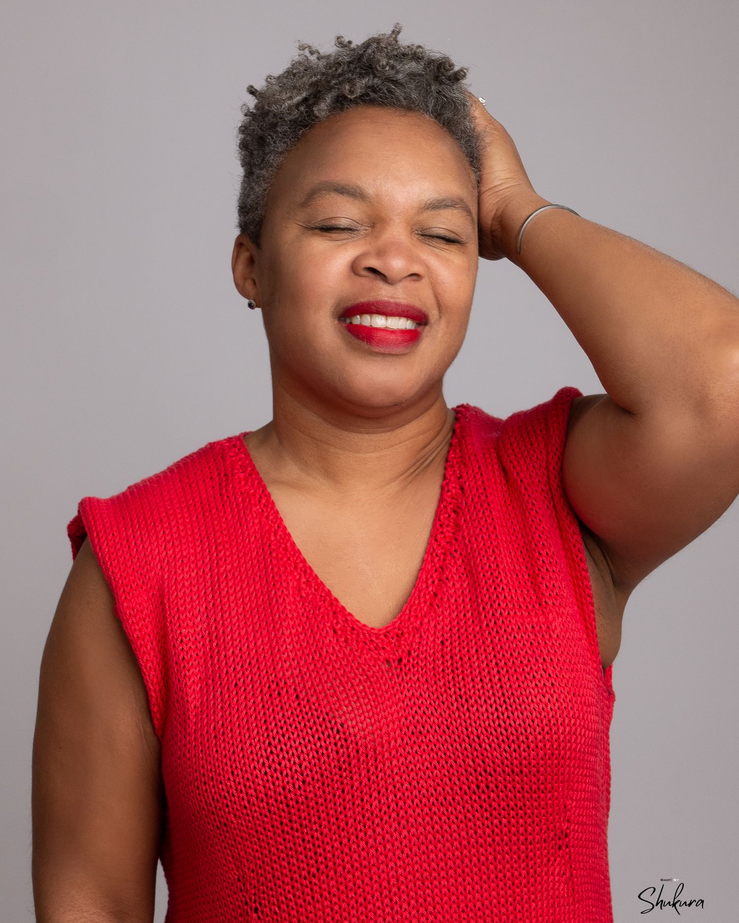 A confident pose in a red sleeveless knit top against a gray studio backdrop.