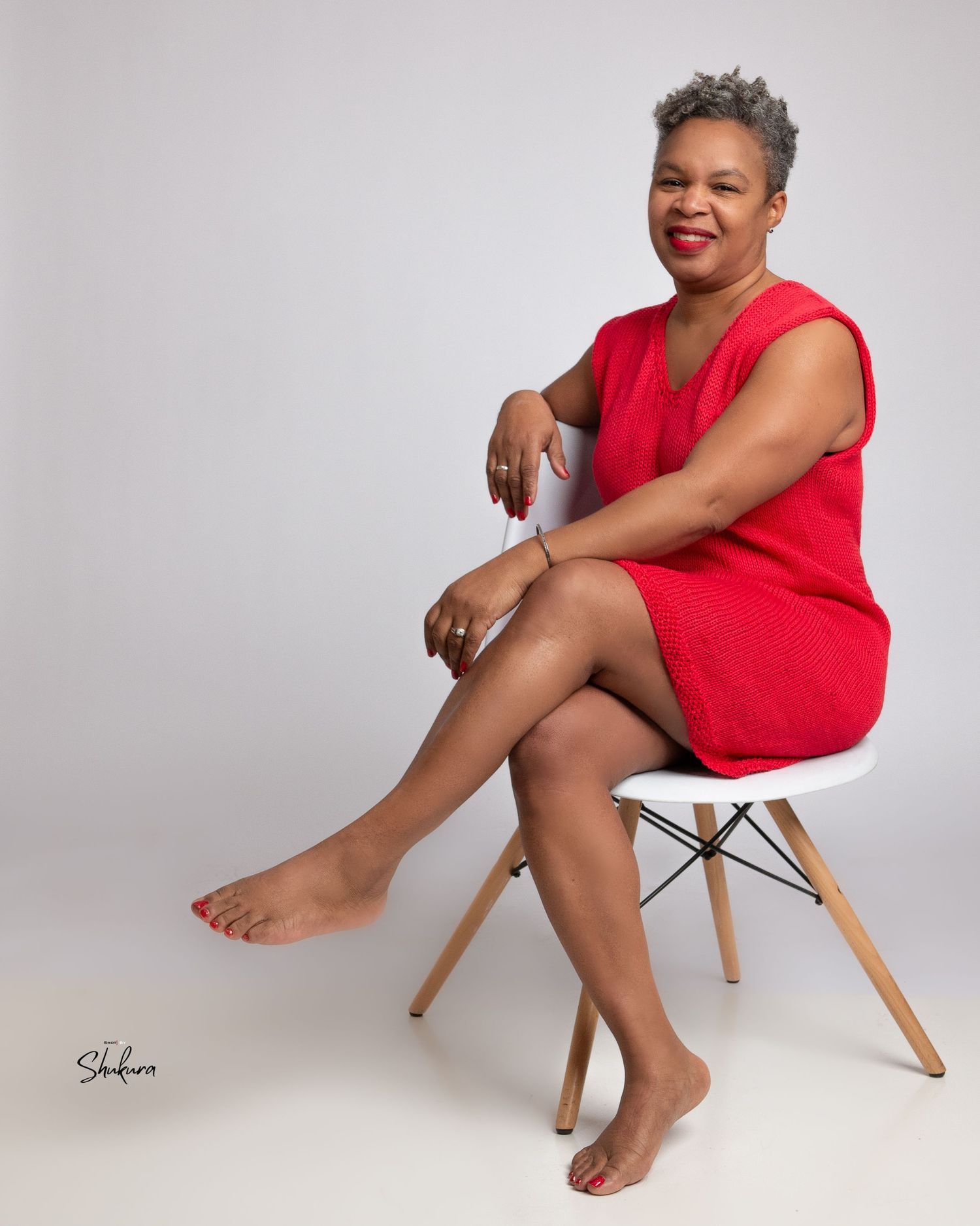 Relaxed studio portrait on a modern chair wearing a red sleeveless dress.