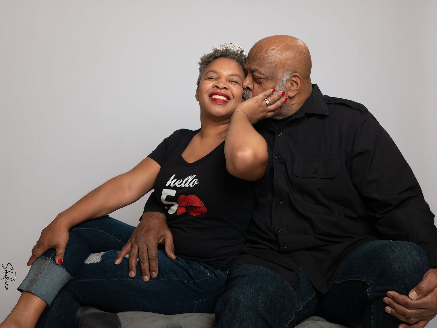 Sweet candid studio portrait of a couple in matching black outfits sharing a playful moment.