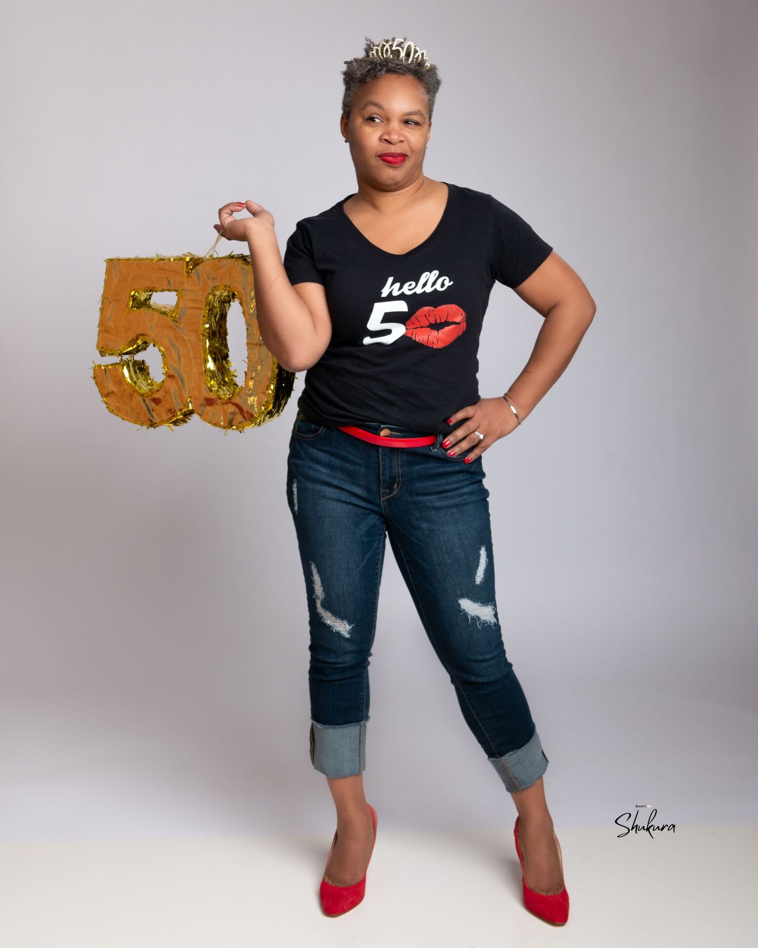 Casual portrait with distressed jeans, red heels and a graphic t-shirt holding a gold prop.