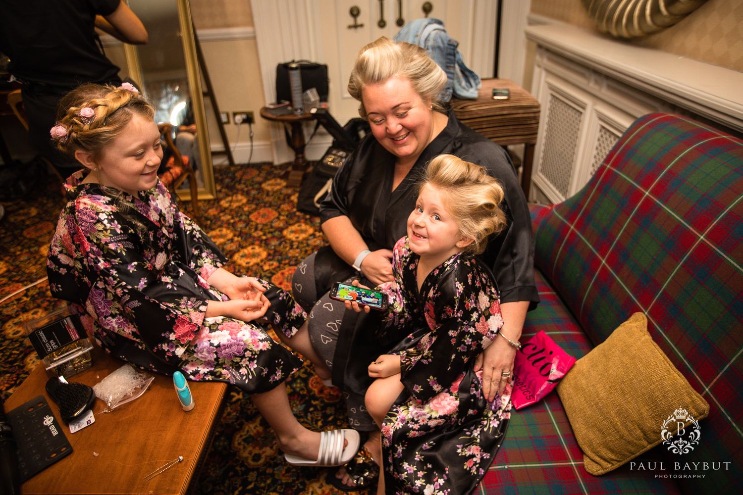 Joyful family moment with matching floral robes on a wood floor during wedding preparations.