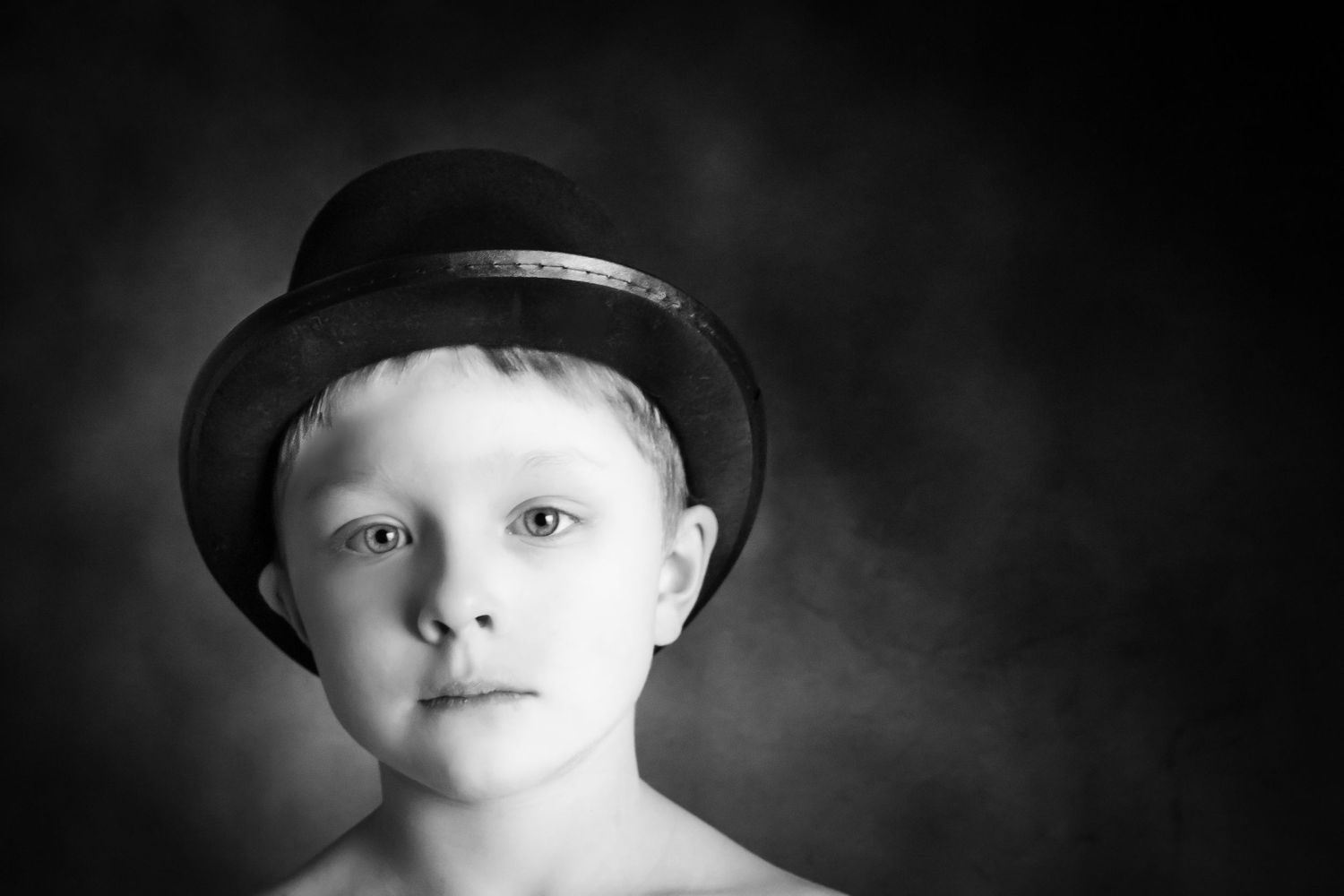 6 year old boy in fine art photo shoot wearing black top hat looking longingly at the camera