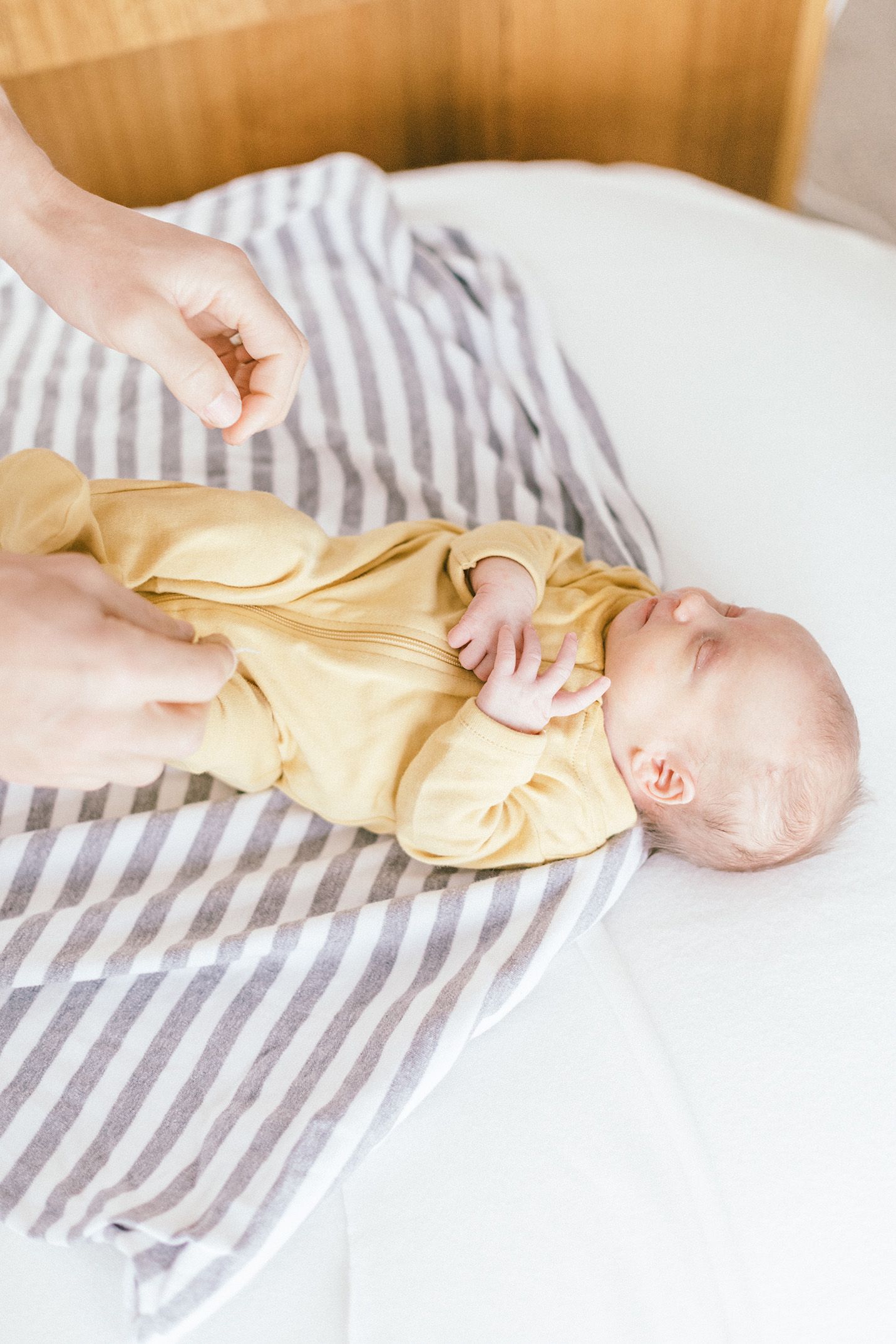 Newborn baby wearing yellow outfit being gently changed on striped blanket.