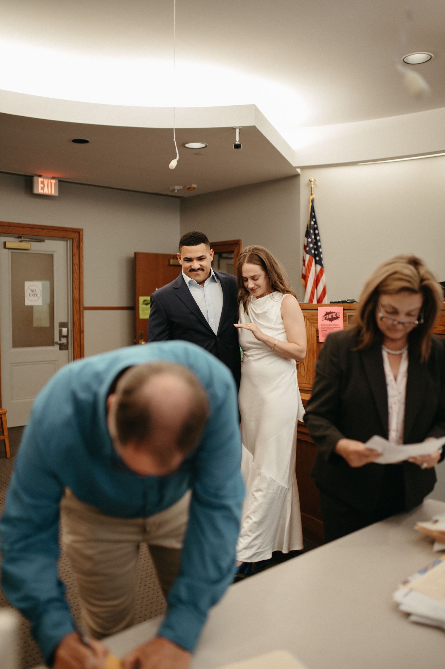 A scene from a courthouse wedding ceremony with attendees gathering around paperwork.
