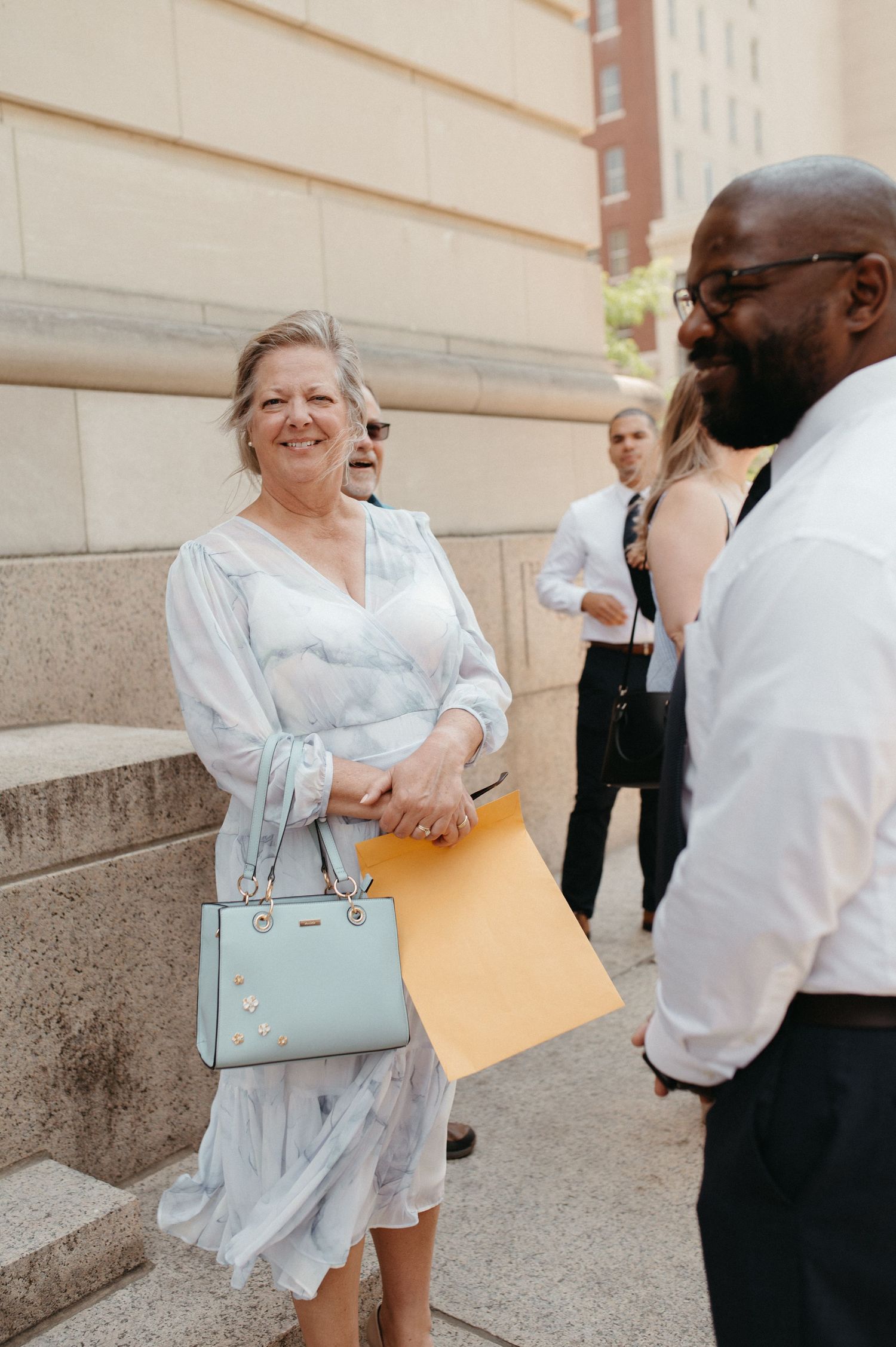 People engaging in casual conversation outside building with woman holding light blue purse.