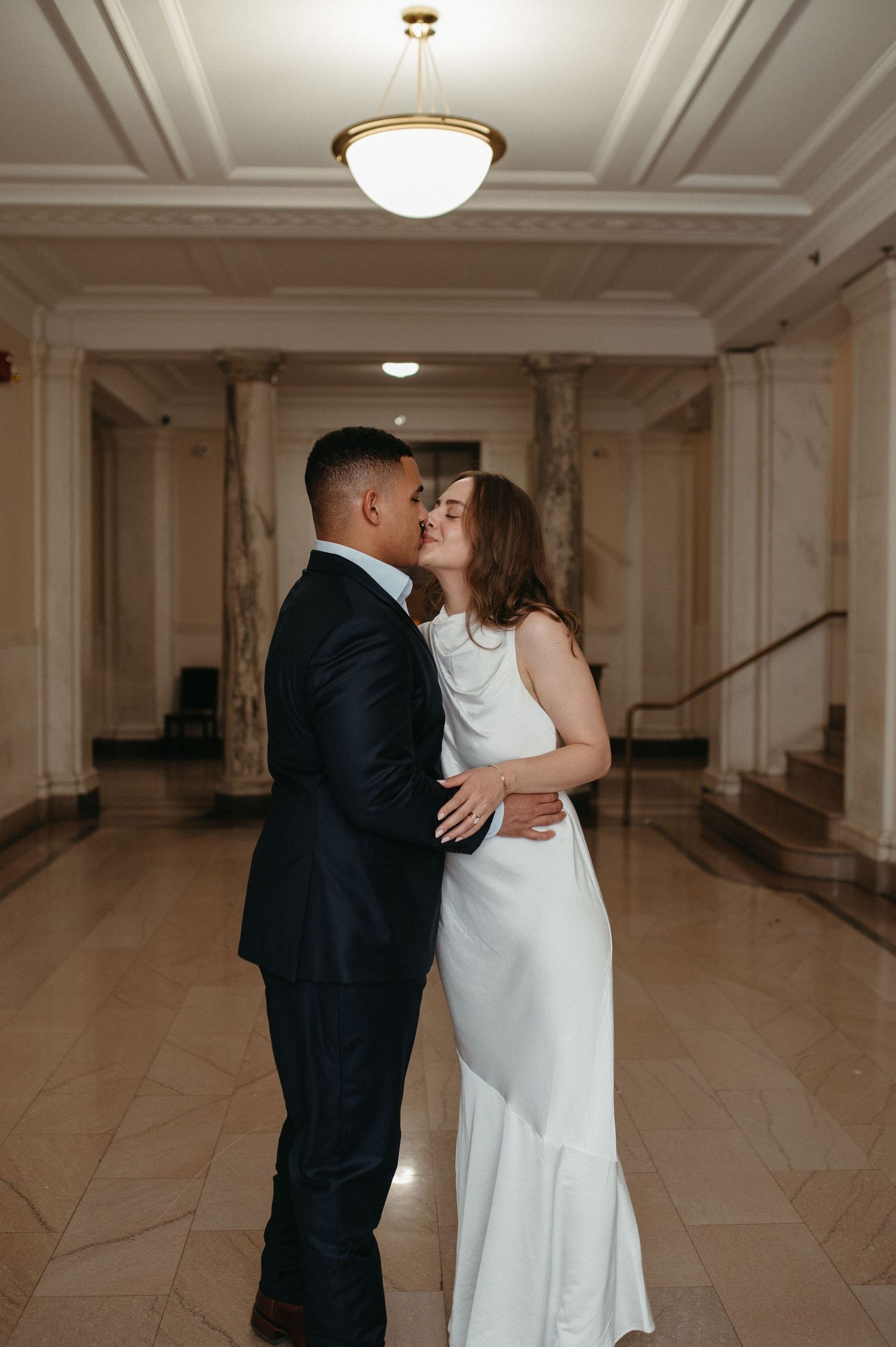 A romantic moment between a couple in formal attire sharing a kiss in a grand hallway.