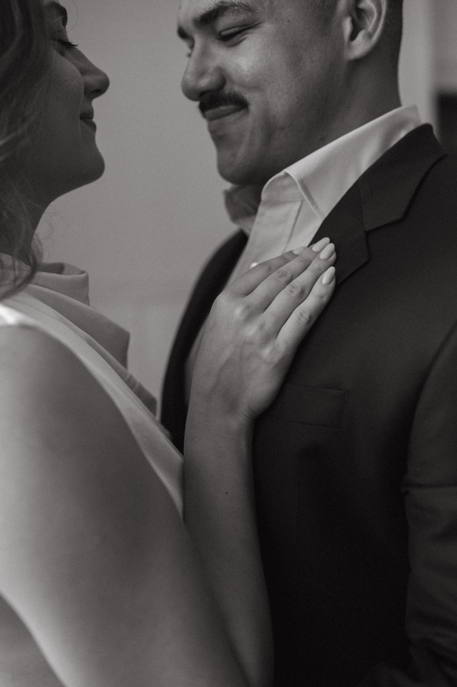 A romantic black and white close-up of a couple embracing, showing tender intimacy in formal attire.