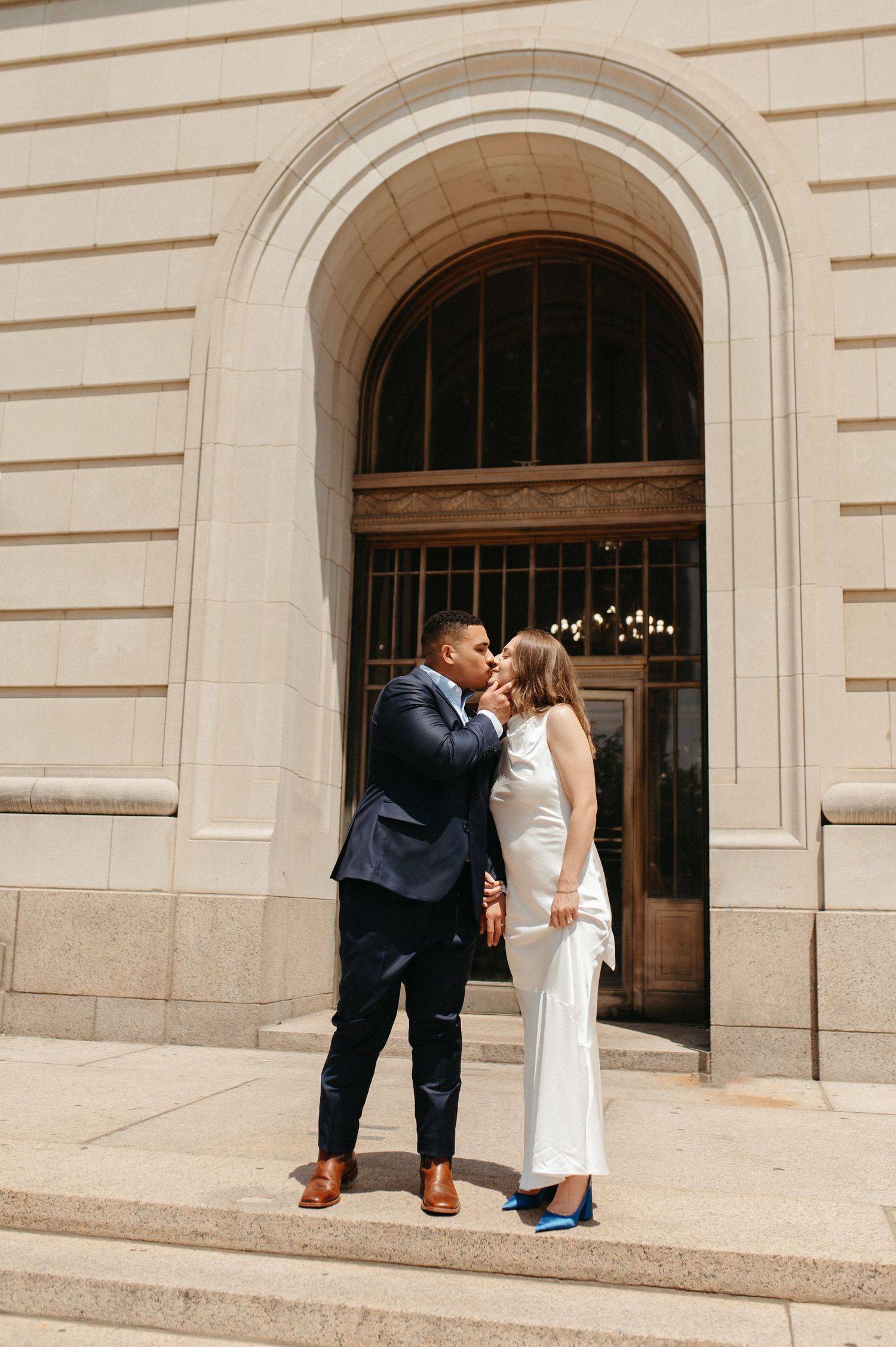 Intimate moment between couple in formal attire on stone steps of classical building.