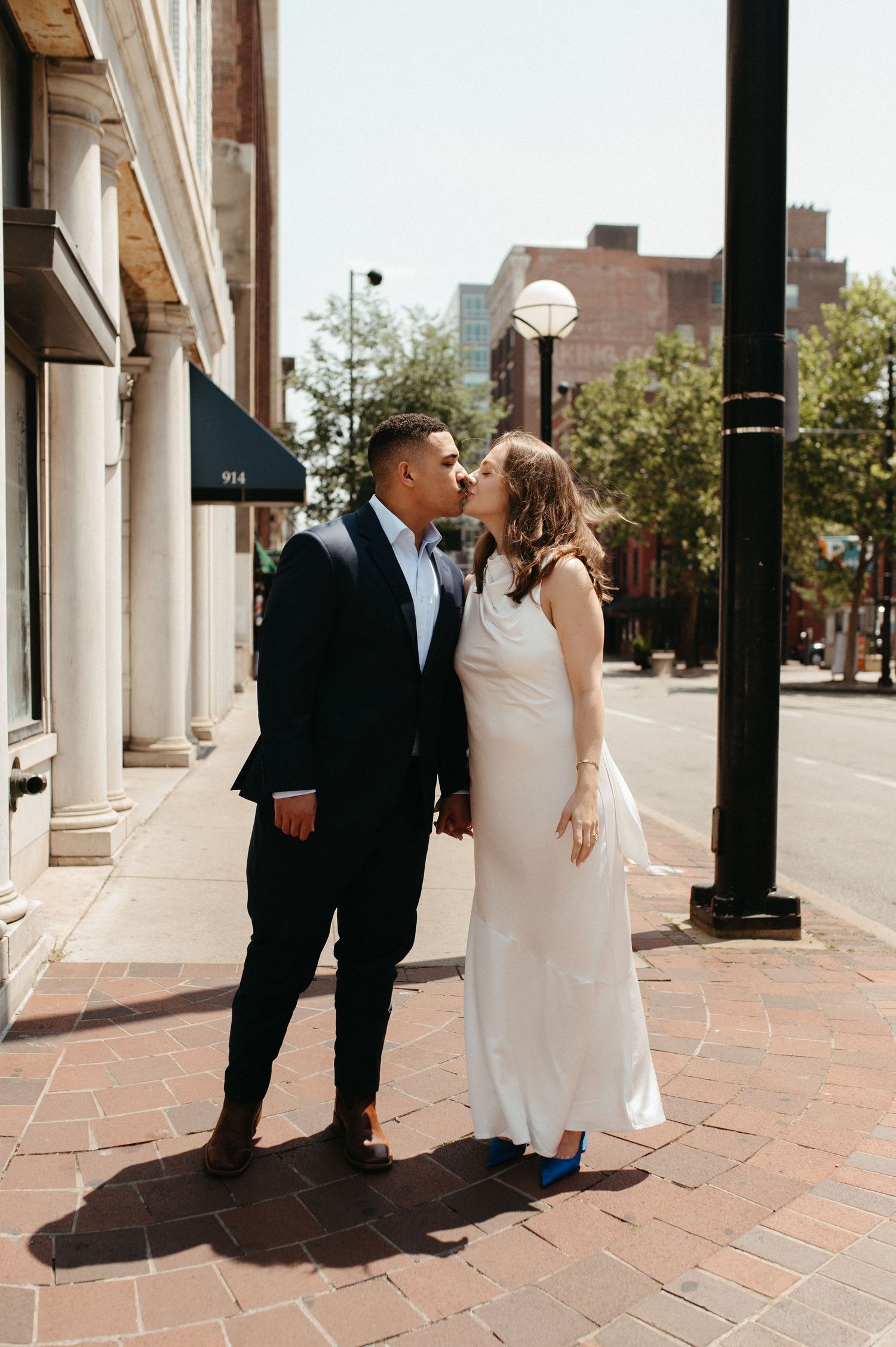 Romantic moment between newlyweds on a brick sidewalk with urban architecture in the background.